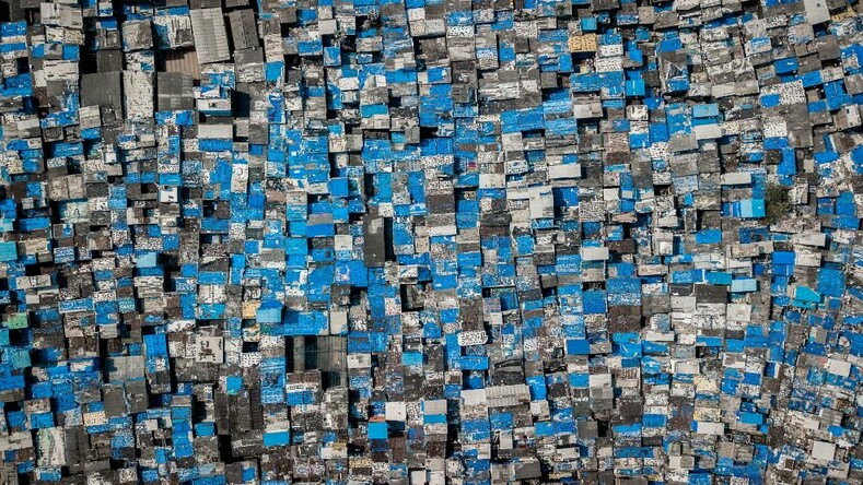 Дхарави, город внутри города, почти полностью сделан из серого бетона. Обитатели трущоб в северных районах Мумбаи используют голубые брезенты для защиты от муссонных дождей. Дома упакованы так плотно, что невозможно увидеть пути между ними сверху.
