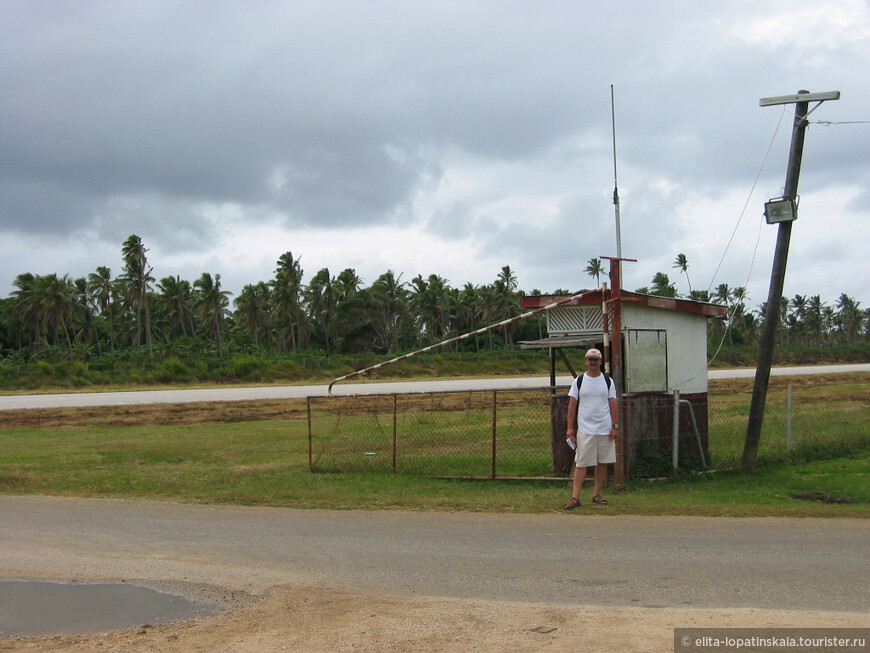 Шлагбаум перекрывающий главную дорогу острова Лифука в месте её пересечения со взлётно-посадочной полосой (на заднем плане) местного аэропорта