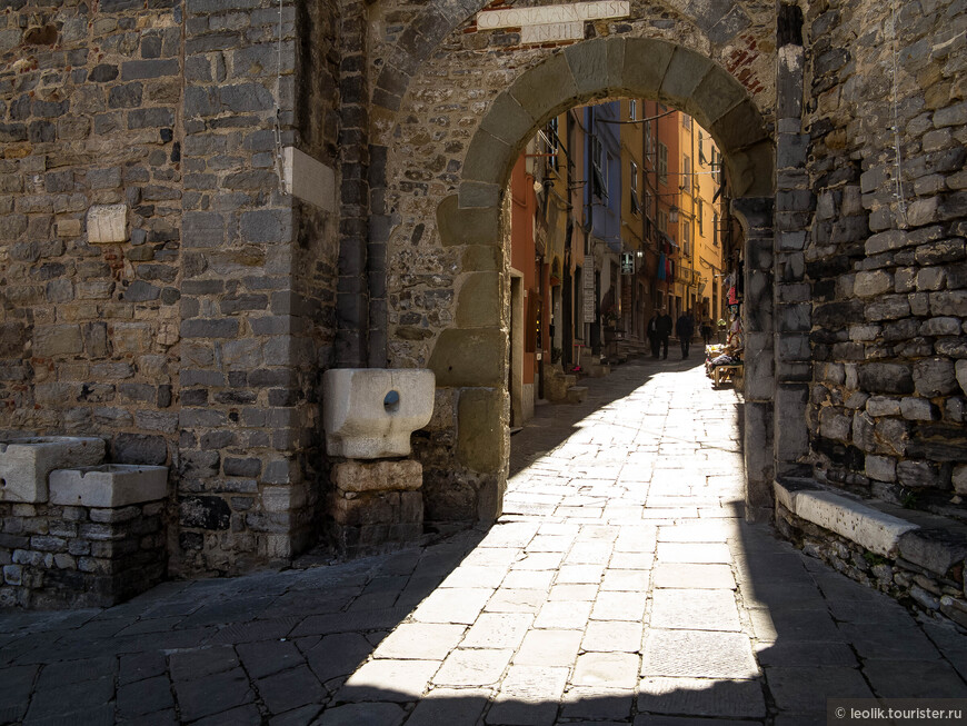 Римские ворота, ведущие на улицу Капеллини (via Capellini) – одну из главных улиц города – были построены в 1113 году. Рядом с ними находится башня, возведенная почти на полвека позже – в 1161 году.