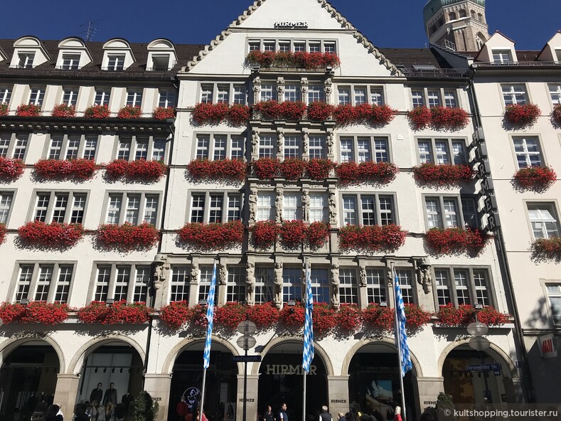 укашенный гераньями фасад семейного мужского магазина Хирмер в Мюнхене