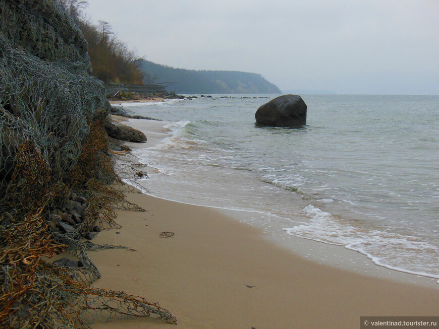 На окраине дикого пляжа в море лежит большой темный камень.