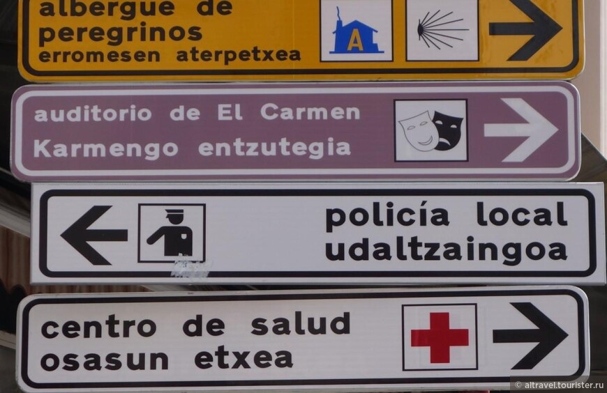 Испанский язык - в первой строчке этих объявлений, баскский – во второй. Сверху вниз указатели на: гостиницу для паломников, концертный зал Кармен, полицию, центр здоровья. 
