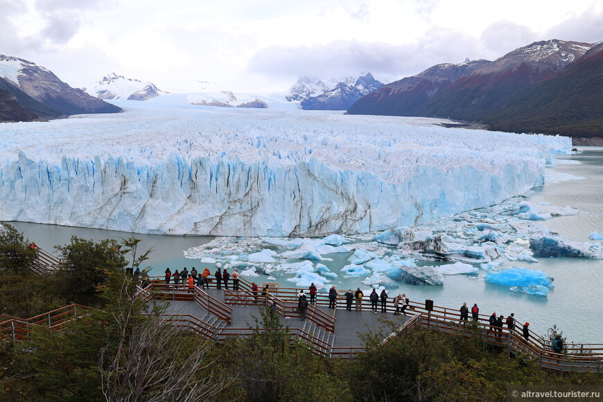 Люди любуются ледником и ждут момента, когда огромные куски льда сорвутся с него и упадут в воду.

