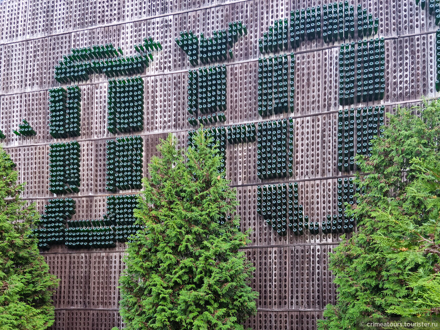 Восточная заводская стена облицована пюпитрами, в которых бутылками выложены слова 'Абрау-Дюрсо'. В настоящее время декоративные туи выросли и закрывают часть букв.