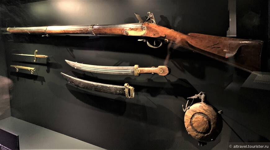 Русское оружие 19-го века, «ходившее» на Аляске: мушкет (вверху), морской кортик с ножнами (слева), кинжал с ножнами (в центре), пороховая фляжка (справа).